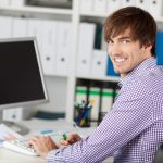 Junger Mann sitzt vor dem Computer. Informatikkaufleute beraten zu allen Software-Fragen. Beruf: Informatikkaufmann/-frau