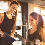 Personaltrainer zeigt Frau Übungen auf ihrem Klemmbrett. Bei diesem Job zählt nicht nur die körperliche Fitness. Beruf: Sport- und Fitnesskaufmann/-frau