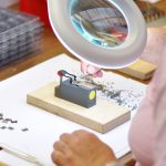 Auf diesem Bild werden Arbeitsbereiche des Feinmechanikers dargestellt. Durch eine Vergrößerungslampe arbeitet ein Feinmechaniker an einem Bauteil, welches vor ihm liegt. Hier ist absolute Präzision gefragt. Beruf: Feinwerkmechaniker/in