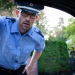 Ein Polizist in blauer Uniform schaut in ein Auto und fragt nach den Fahrzeugpapieren. Ein freundlicher Umgang mit Menschen und ein hohes Maß an Konfliktfähigkeit sind für diesen Beurf von Vorteil. Beruf: Polizeivollzugsbeamte/r (im mittleren Dienst)