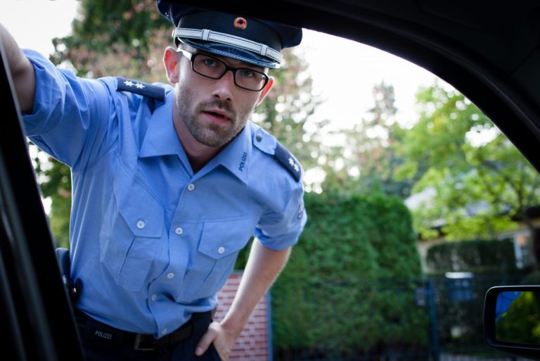 Ein Polizist in blauer Uniform schaut in ein Auto und fragt nach den Fahrzeugpapieren. Ein freundlicher Umgang mit Menschen und ein hohes Maß an Konfliktfähigkeit sind für diesen Beurf von Vorteil. Beruf: Polizeivollzugsbeamte/r (im mittleren Dienst)